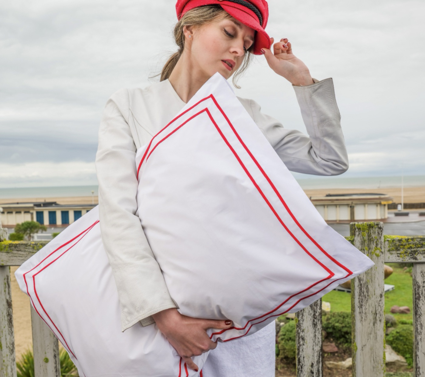 Femme en casquette rouge tenant un coussin blanc liseré rouge