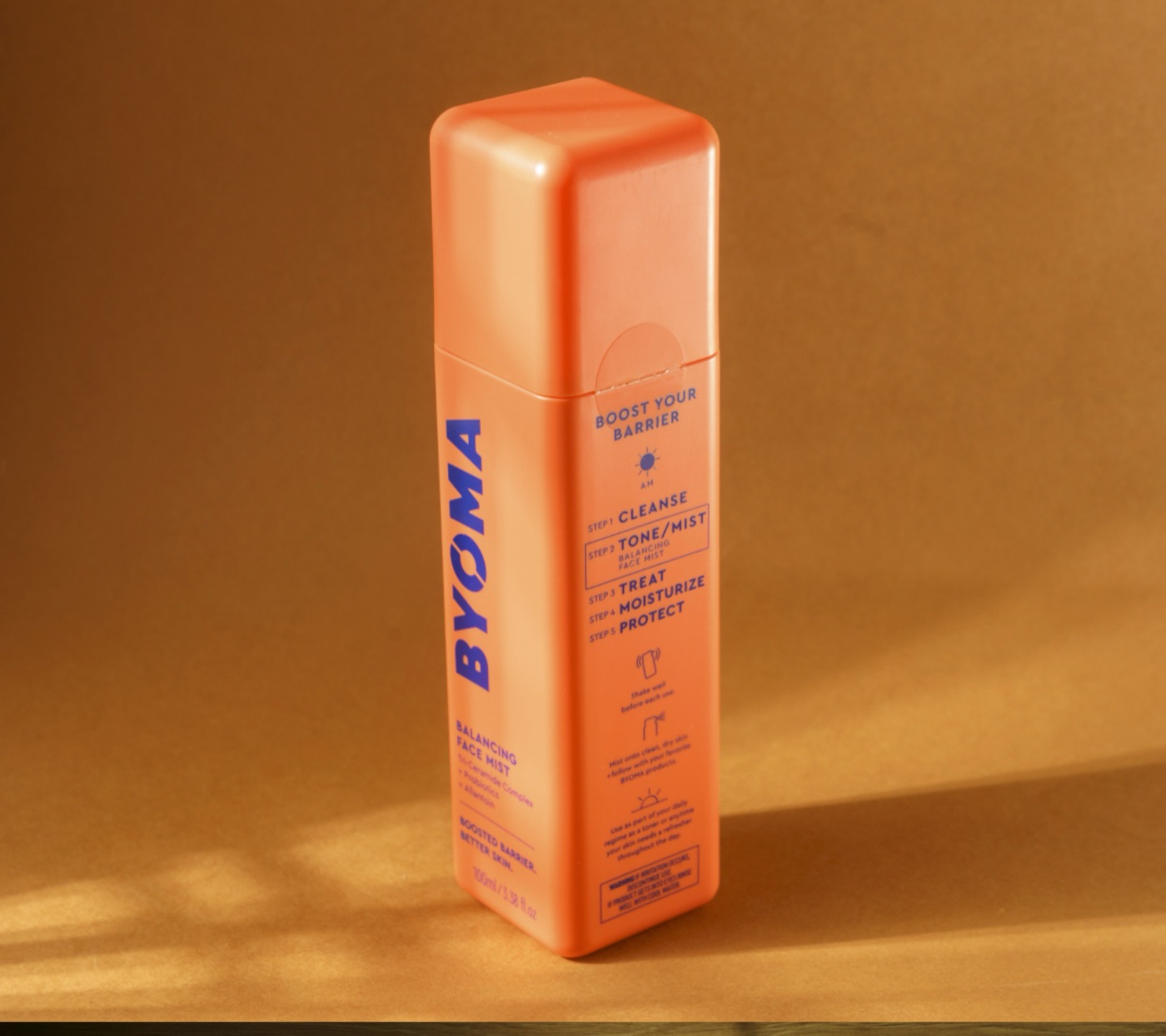 Packshot d'un flacon cosmétique orange sur fond ocre