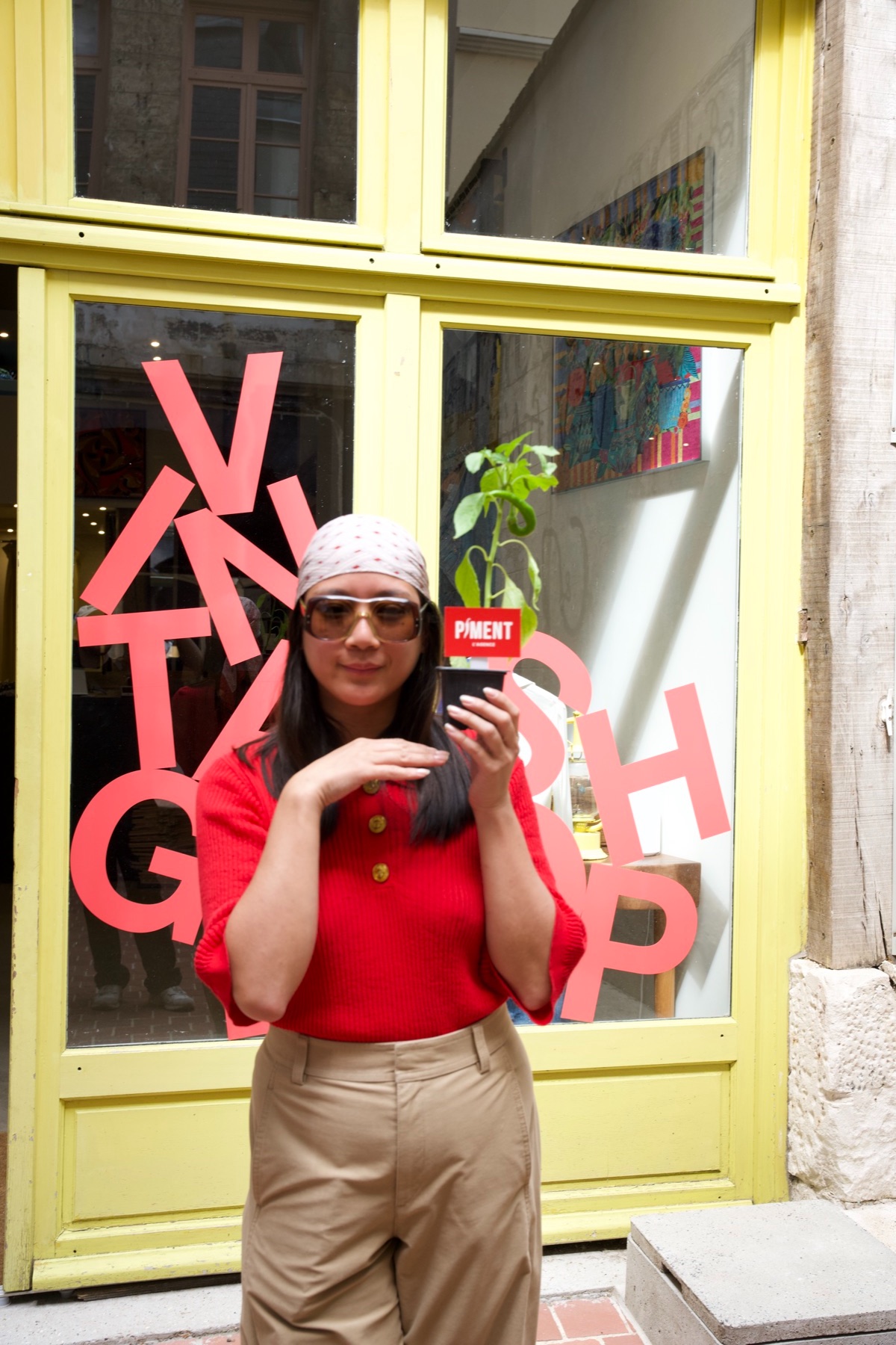 Une commerçante souriante tient son plant de piment devant sa boutique